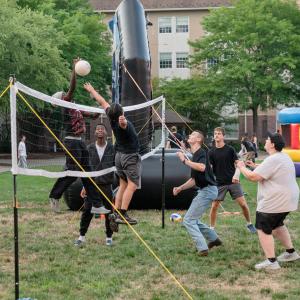 Students play voleyball on a lawn.