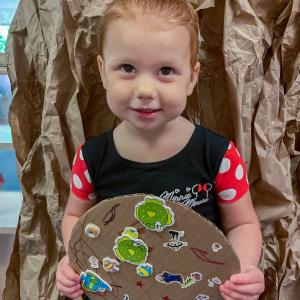 A small child holds a cardboard circle on which she has colore and placed stickers.