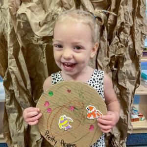 A small child holds a cardboard circle on which she has colore and placed stickers.