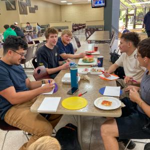 A group of students eating at a table in Penn College's Keystone Dining Room write on blank sheets of paper.