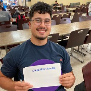 A student holds up a purple dot and a sheet of paper with the handwritten word "cheeseburger."