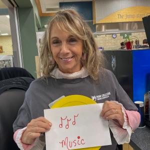 A woman holds up a yellow circle and a sheet of paper on which she has drawn musical notes and written the word "music."