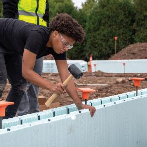Shanya M. Allen, a building construction technology student, taps a second course of insulated concrete forms to interlock with the first.