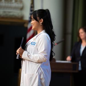 A smiling woman stands on stage holding a diploma folder.