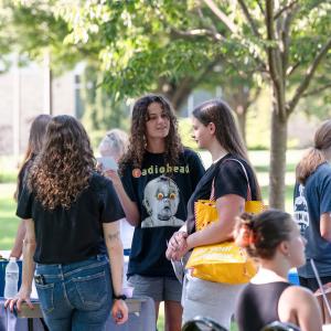A student holding an index card chats with other students near a table on a Penn College sidwalk. Also visible are students speaking with people at other tables.