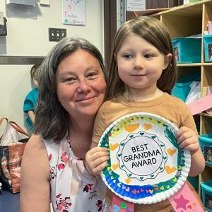 A woman and child pose with a medal made by the child. The medal reads "Best Grandma Award."
