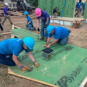 Volunteers in blue T-shirts and hard hats add sheathing to a gable end truss.