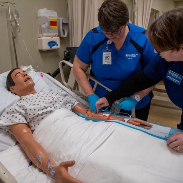 Instructor assisting nursing student with mannequin