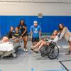 students pose with a hospital bed, crutches and a wheelchair