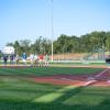 A group of Penn College representatives stands at mid-field at Volunteer Stadium, while a young catcher and Dugout, Little League's mascot, stand near home plate.