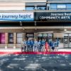 A group of people in business attire gathers on a red carpet beneath the Journey Bank Community Arts Center marquee.