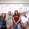 Six young adults stand in front of a white board, on which a printed research poster is hung.