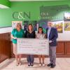 Four people in business attire hold a giant check in the lobby of a C&N branch.