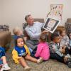 Penn College President Mike Reed sits on the floor. He is surrounded by toddlers and is looking at an oversized hand-made card.