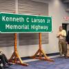 Inside Penn College's Thompson Professionald Development Center, people on either side of a highway sign applaud. The sign is hanging on wooden posts.