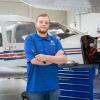 A student stands with arms crossed in front of an airplane and large toolbox.