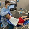In Penn College's Dental Hygiene Clinic, a child lies back in a dental chair while a student wearing a medical gown and mask examines the child's teeth.