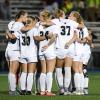 Penn College women's soccer players huddle together arm-in-arm on the field.