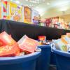 Bins heaped full of nonperishable food sit in front of a long table, also filled with nonperishable food items.