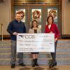 Three people pose with an oversized check in the Community Arts Center lobby.