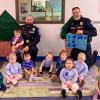 Toddlers sit on a rug in front of two Penn College Police officers. One his holding a handmade thank you card.