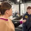 A woman holds a microphone to another woman. They are surrounded by manufacturing equipment in Penn College's Lycoming Engines Metal Trades Center.