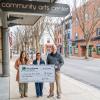 Three people hold a large check under a Community Arts Center sign outside the building. Williamsport's West Fourth Street is visible behind them.