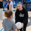 A college athlete smiles widely while holding a soccer ball and interacting with a girl.