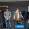A man speaks from a podium while Penn College students and faculty stand behind him on the porch of a house.