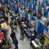 Overhead view of a gym filled with several rows of employer booths. Students walk among the booths and talk with the employers.