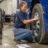A high school student examines the wheel of a big rig truck.