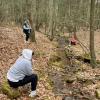 Students sit along a run in a woods.