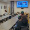 People sitting around a long table in Penn College's Center for Career Design focus on a large video screen that shows a virtual meeting in progress.