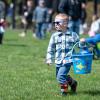 A child un sunglasses carries a bucket through a Penn College lawn, looking for eggs, as children in the background do the same.