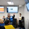 An emergency management student wearing a blue vest speaks and motions toward a video screen on the wall in Penn College emergency management classroom. Other students in yellow, white and blue vests are seated at tables.