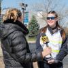 A woman with a television microphone talks with a student wearing a white emergency services vest.
