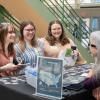 Three students smile as they stand across the table from an employer in the college's Advanced Technology & Health Sciences Center atrium.