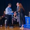 A student accepts a white rose while walking across Penn College's Klump Academic Center Auditorium stage.
