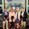 Six people wearing dress clothes and holding plaques.