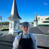 A student in a chefs uniform stands in Churchill Downs with its famous twin spires behind her.