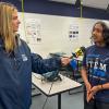 A television reporter holds a microphone up to a middle school student wearing a Penn College STEMFest T-shirt.