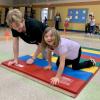 A college student and elementary school student crawl across a gym mat.