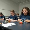Middle school girls sit at a classroom table building Lego robots.