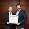 Two men in suits hold a framed certificate.
