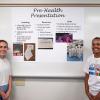 Two students stand in front of a poster that is titled "Pre-Health Presentation."