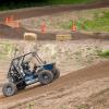 A student-built Baja vehicle races up a hill on a dirt track.