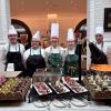 Five Penn College students in chefs uniforms stand behind a table of elaborate desserts in a Churchill Downs dining venue that has white brick walls.
