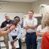 In Penn College's injection molding lab, people in safety goggles listen as an instructor holds up pieces of plastcs. Injection molding machines are visible in the background.