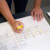 Closeup of a hand holding a yellow higlighter marker over an HVAC blueprint.