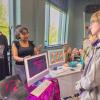 A Penn College student standing behind a display table that shows a variety of her graphic design work speaks to high school students.